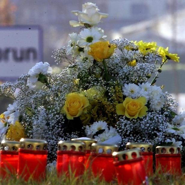 Kerzen und Blumen im Vordergrund, dahinter Ortsschild von Kaprun