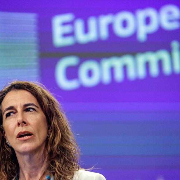 Eine Frau mit welligem Haar spricht vor dem Hintergrund der Europäischen Kommission.