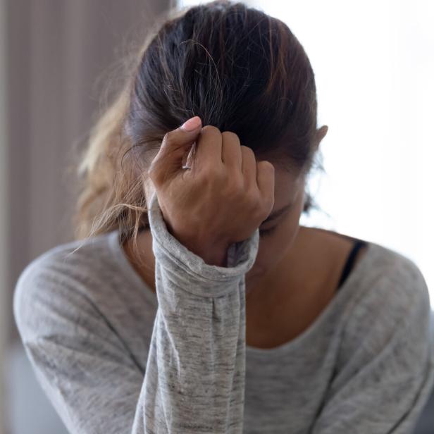 Eine Frau sitzt mit gesenktem Kopf und hält sich die Stirn, wirkt nachdenklich oder besorgt.