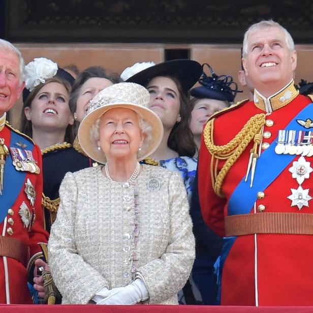 Königin Elisabeth II. mit Prinz Charles und Prinz Andrew auf einem Balkon, alle lächeln.