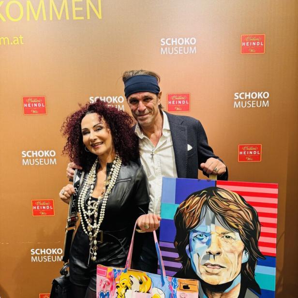 Zwei Personen posieren vor einer braunen Wand mit Pop-Art-Gemälden von Mick Jagger und Marilyn Monroe.