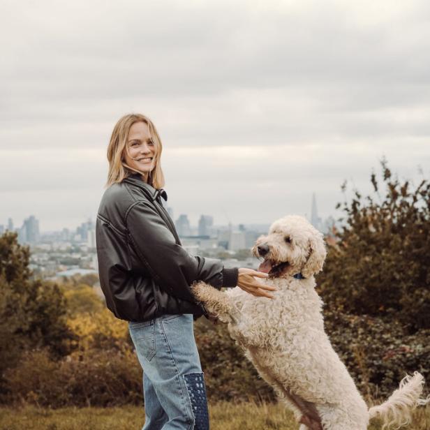 Ein beiger, wuscheliger Hund, wie er mit Moderatorin Mirjam Weichselbraun auf einer Wiese spielt
