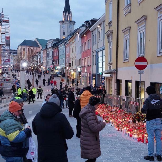 Viele Menschen versammeln sich an einer abgesperrten Straße, umgeben von zahlreichen Kerzen und Blumen zum Gedenken.