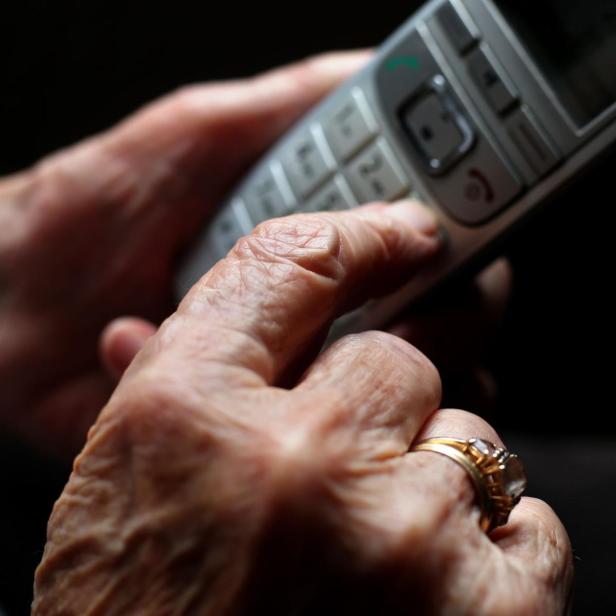 Eine ältere Hand mit Ring tippt auf die Tasten eines schnurlosen Telefons.