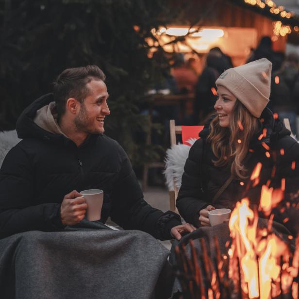 Ein Mann und eine Frau wärmen sich an einem Lagerfeuer. 
