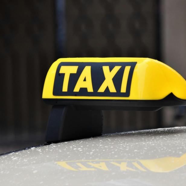 Gelbes TAXI-Dachzeichen auf einem Auto, im Hintergrund unscharf.