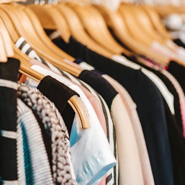 Mehrere bunte Kleidungsstücke hängen ordentlich auf Holzkleiderbügeln an einer Stange.