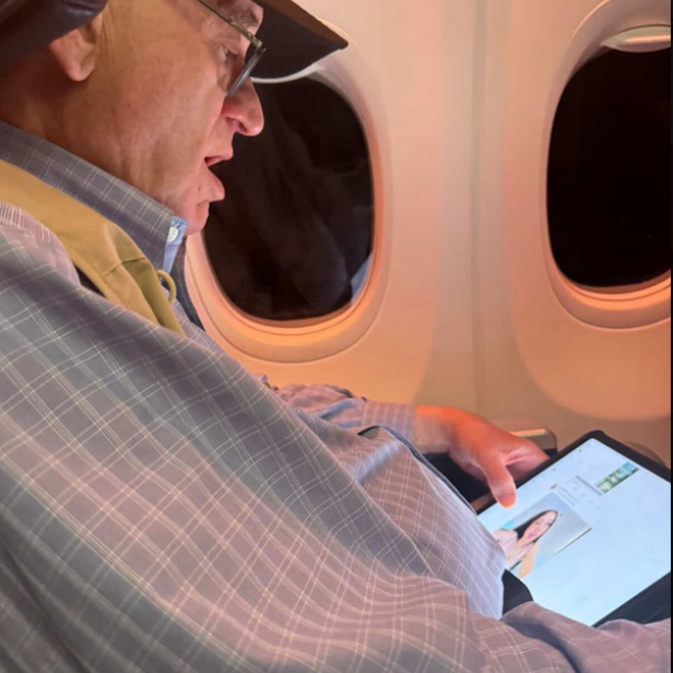 Brad Sherman sitzt im Flugzeug und betrachtet auf seinem Tablet ein Bild einer Frau in Unterwäsche.