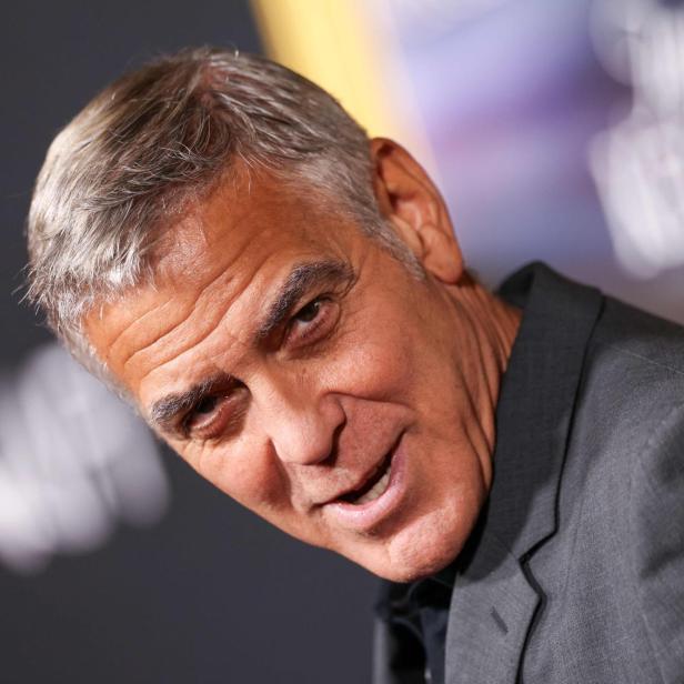 George Clooney lächelt in einem grauen Anzug vor einem unscharfen Hintergrund.