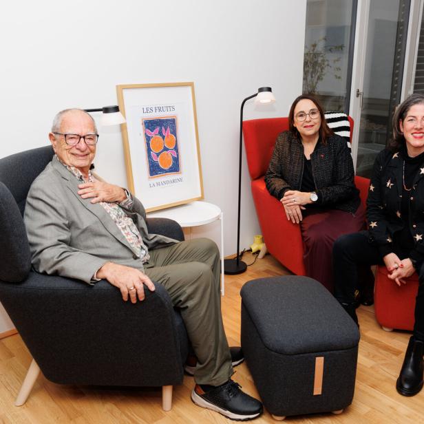 Drei Personen sitzen entspannt in einem modern eingerichteten Raum mit farbigen Sesseln und einem gerahmten Kunstwerk.