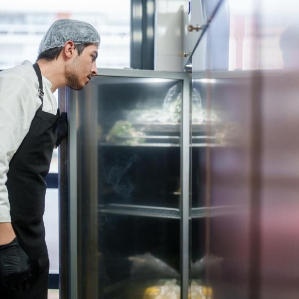 Ein Mann schaut in einer Profiküche in einen Kühlschrank. 