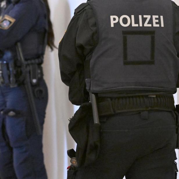 Eine Aufnahme von mehreren uniformierten Personen. Ein Mensch steht mit dem Rücken zur Kamera, auf der Weste ist "Polizei" zu lesen.