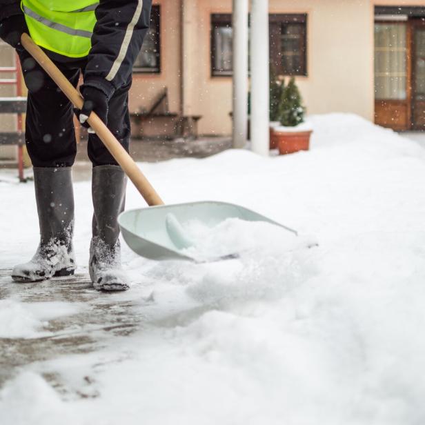 Mann schaufelt Schnee vom Gehsteig