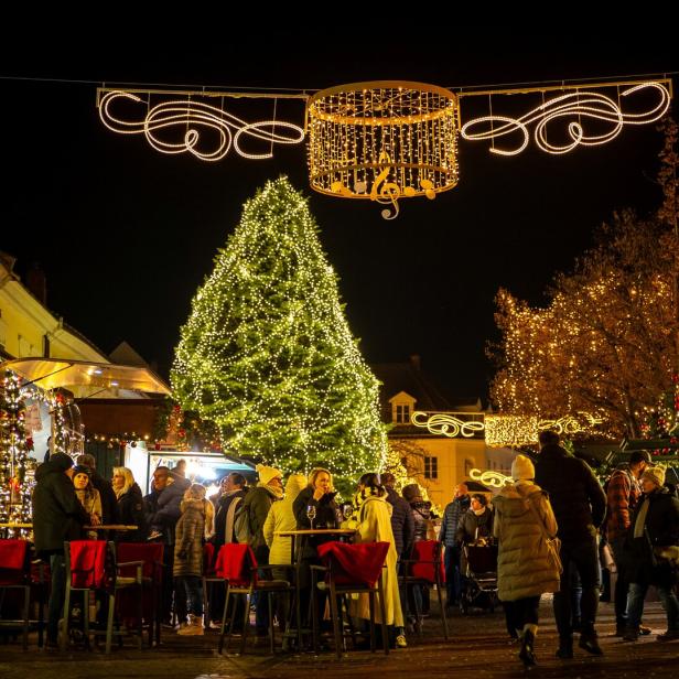 Menschen genießen einen festlich beleuchteten Weihnachtsmarkt mit geschmücktem Tannenbaum und Lichterketten bei Nacht.