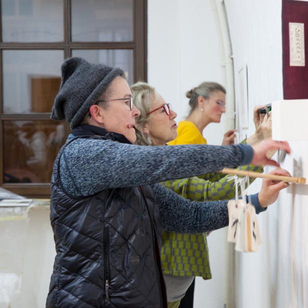 zwei Frauen befestigen Bilder an einer Wand