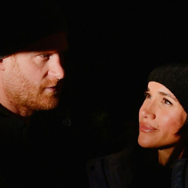 Harry und Meghan, beide mit Mützen, schauen einander im Dunkeln an.