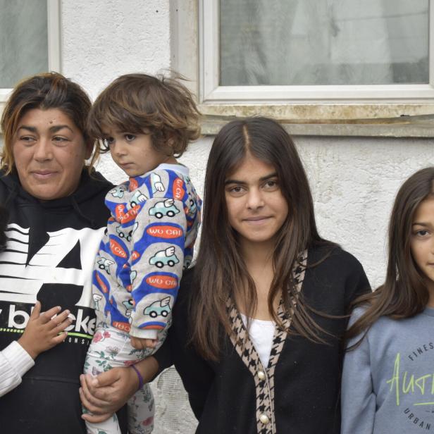 Eine Mutter mit ihren vier Kindern steht vor einer weißen Hauswand.