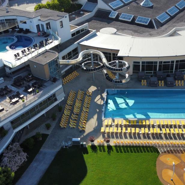 Draufsicht auf ein Schwimmbad mit Liegestühlen, Rutsche und dem Schriftzug "Allegria" auf einem Gebäude.