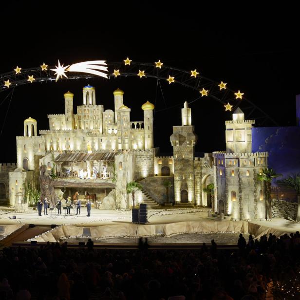 Bühnenbild mit hell beleuchteten, turmähnlichen Strukturen und einer Sternenbogen-Dekoration mit einem leuchtenden Kometen darüber.