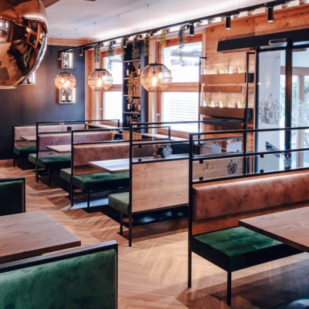Innenansicht eines Restaurants mit Holzdecken und grünen Sitzbänken.