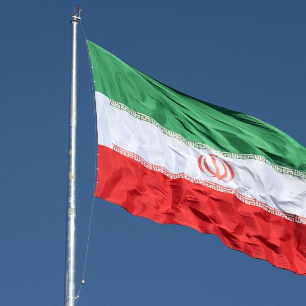 Die iranische Flagge weht vor blauem Himmel.