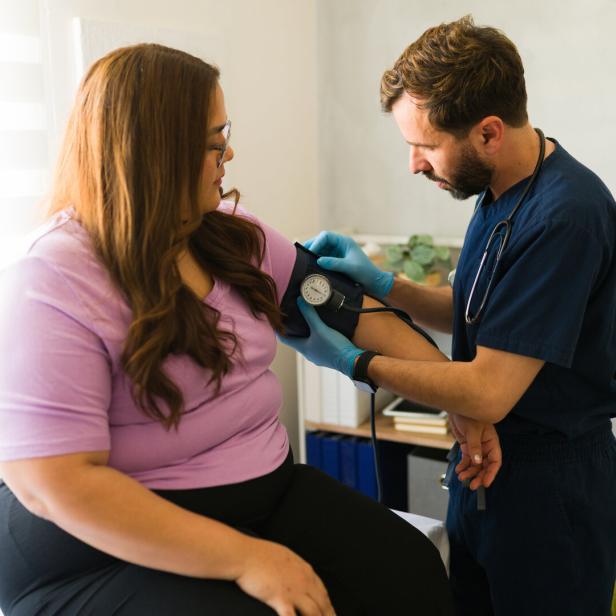 Ein Arzt misst Blutdruck bei einer Frau mit Übergewicht.