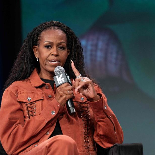 Michelle Obama mit Zöpfen spricht in ein Mikrofon mit dem SXSW-Logo und gestikuliert.
