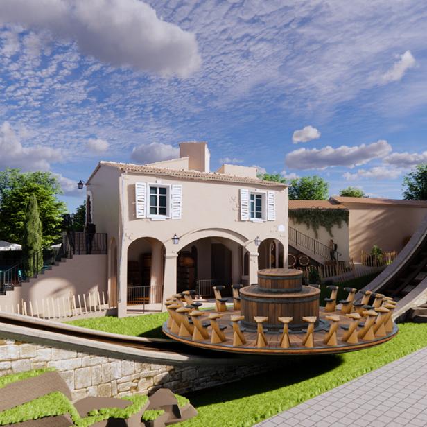 Eine runde Freizeitpark-Attraktion mit Sitzplätzen fährt vor einem mediterranen Gebäude und einer steilen Schienenrampe.