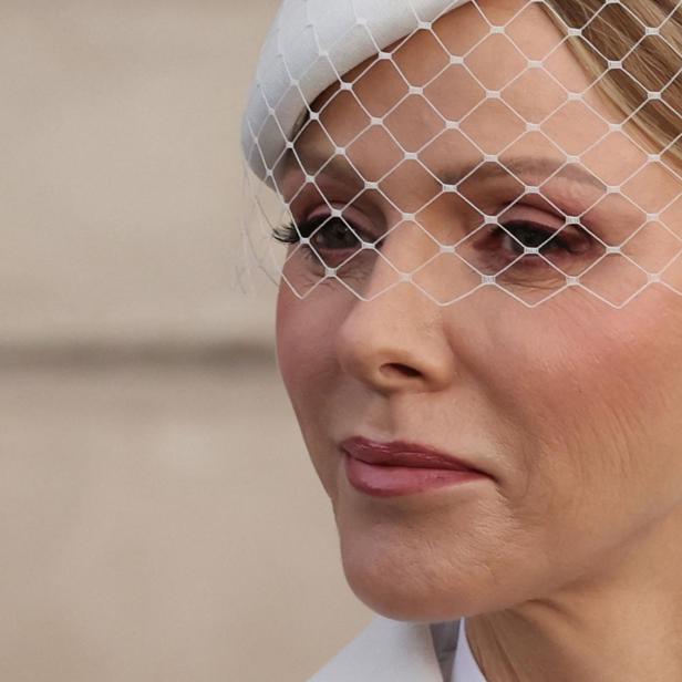 Charlene von Monaco mit blonden Haaren trägt einen weißen Hut mit Schleier und einen Diamantohrring.