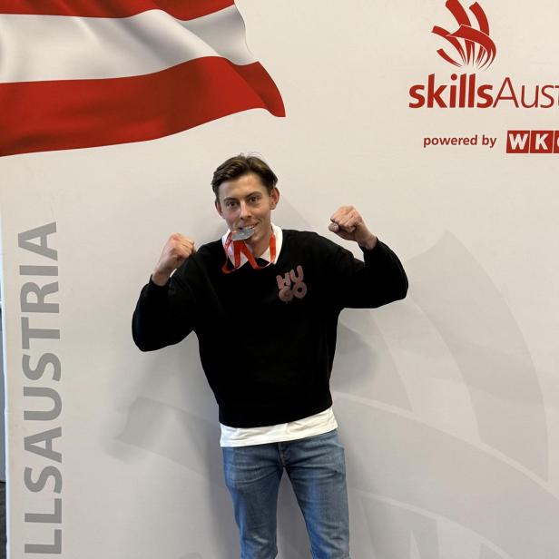 Junger Mann mit Silbermedaille vor SkillsAustria-Logo und österreichischer Flagge.
