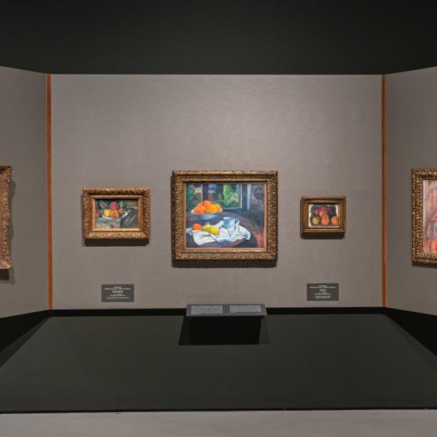Sechs gerahmte Gemälde an einer Museumsmauer, darunter Stillleben mit Blumen und Früchten sowie ein Aktbild, alle in goldfarbenen Rahmen.