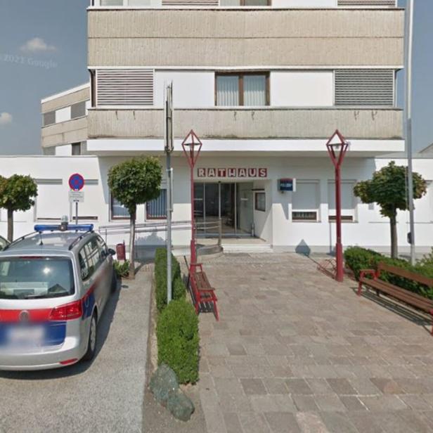 Vor dem Eingang eines Rathauses stehen zwei Polizeiautos, Bänke und kleine Bäume säumen den Weg.