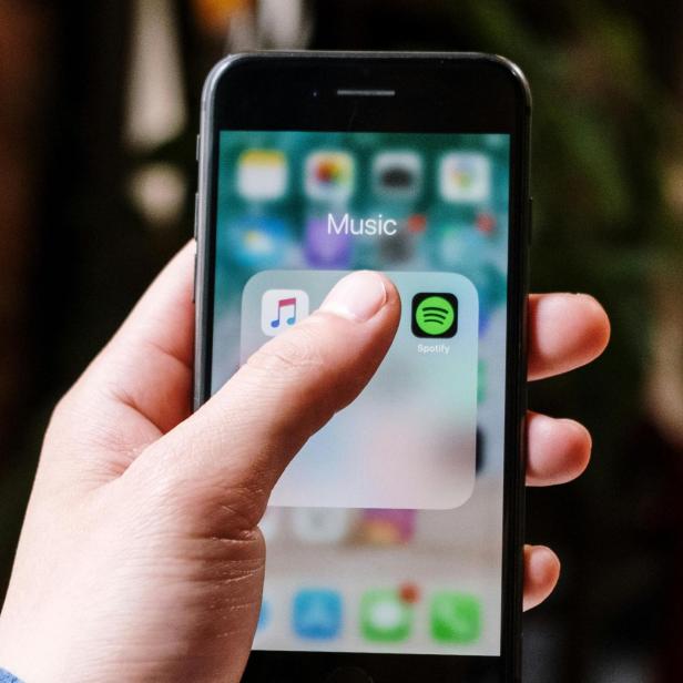 Hand hält Smartphone mit geöffnetem Musik-Ordner und sichtbarem Spotify-Icon.
