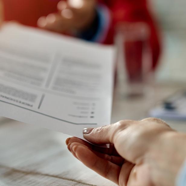 Eine Hand überreicht ein Dokument an eine andere Person bei einem Gespräch am Tisch.