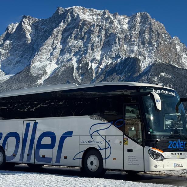 Ein Reisebus von Zoller Reisen vor verschneiter Bergkulisse bei strahlend blauem Himmel.