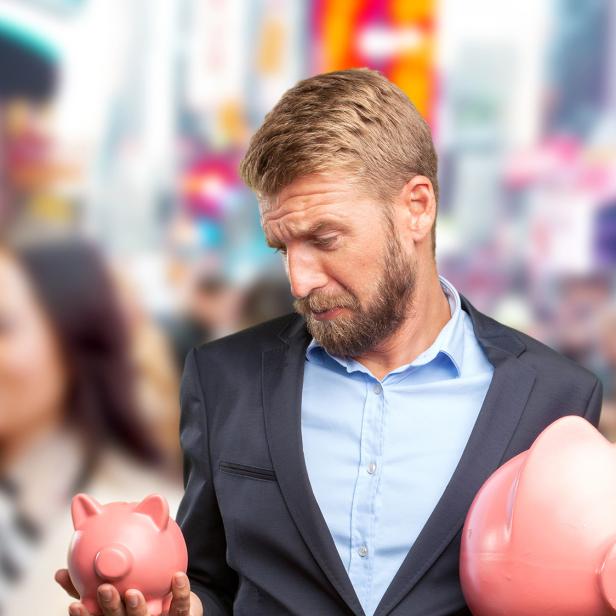 Mann im Anzug blickt besorgt auf zwei unterschiedlich große Sparschweine in den Händen.