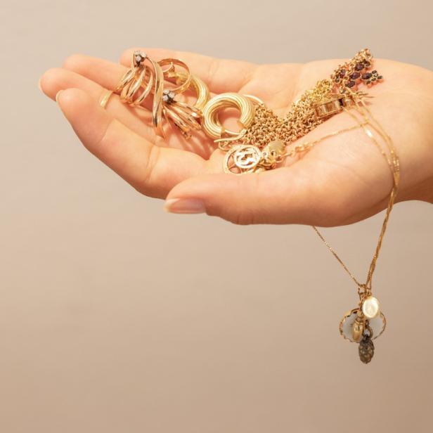 Eine Frauenhand hält einige goldene Schmuckstücke in der Hand.