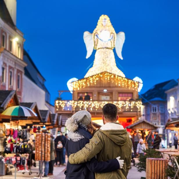 Paar steht in einem Weihnachtsdorf vor einem beleuchteten Engel