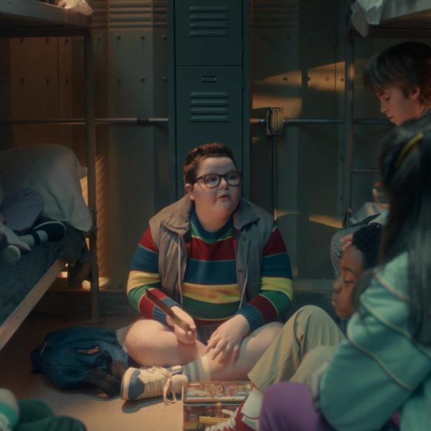 Mehrere Kinder sitzen in einem Schlafsaal im Kreis auf dem Boden zwischen Etagenbetten und unterhalten sich.