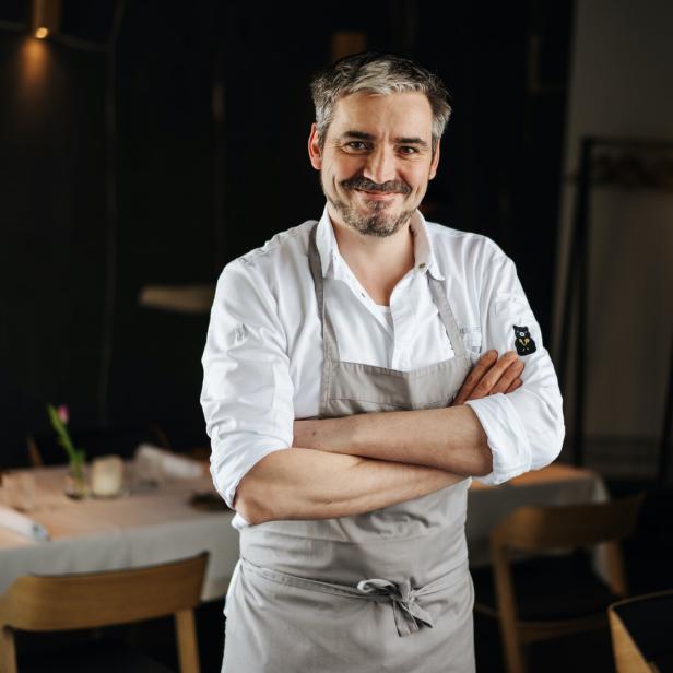 Manuel Ressi, der Koch vom Bärenwirt,  mit verschränkten Armen steht vor einem gedeckten Tisch.