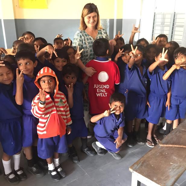 Eine Gruppe Kinder in blauen Schuluniformen posiert mit einer Frau und einem Jungen mit "Jugend Eine Welt"-Shirt.