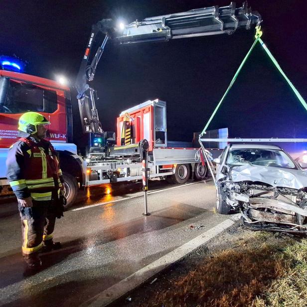 Ein Feuerwehrmann überwacht, wie ein Kran ein stark beschädigtes Auto bei Nacht von der Straße hebt.