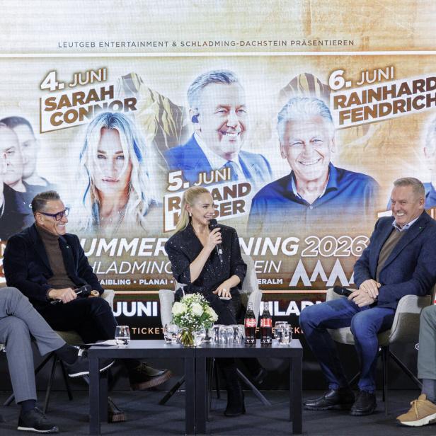 Vier Männer und eine Frau sitzen auf Bühne vor Plakat