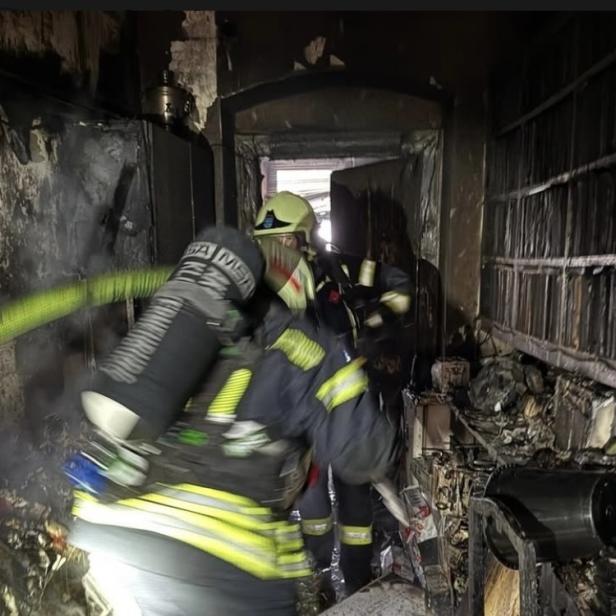 Feuerwehrleute mit Atemschutzgeräten löschen einen stark verbrannten Raum in einem Mehrparteienhaus in Klosterneuburg.