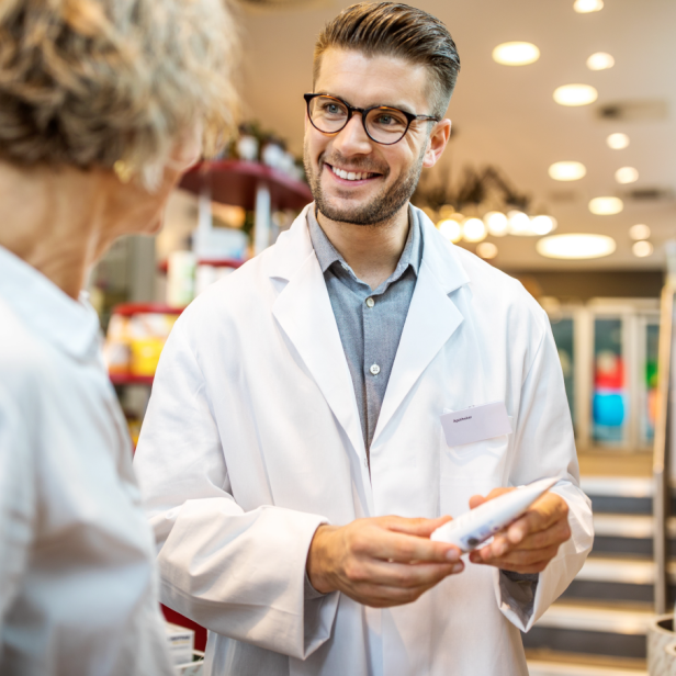 Ein Apotheker berät in einer Apotheke und hält ein Produkt in der Hand. 