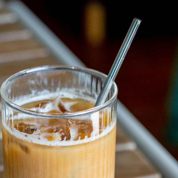 Glas mit Iced Coffee und einem Glasstrohhalm steht auf einem Holztisch