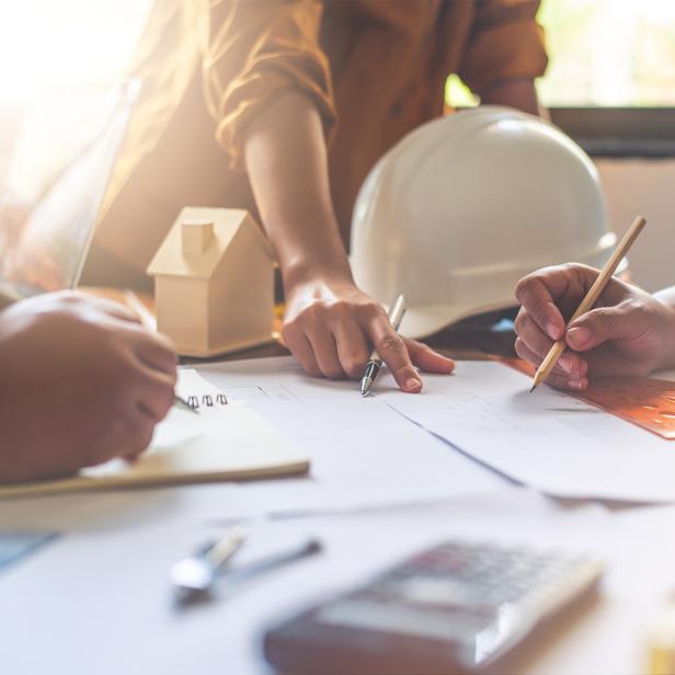 Mehrere Personen arbeiten gemeinsam an Bauplänen und Modellen auf einem Tisch.