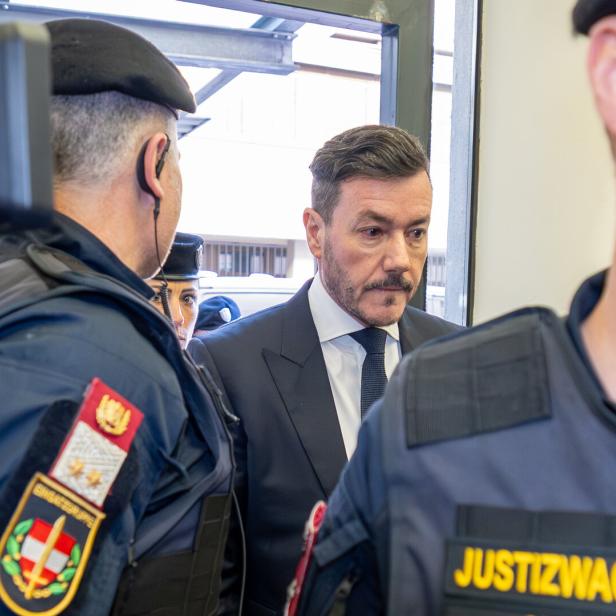 Rene Benko wird von Justizwachebeamten flankiert.