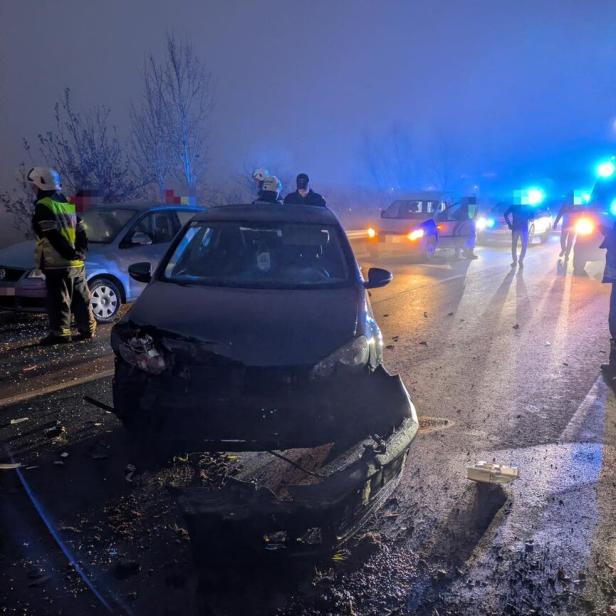 Ein Auto mit stark beschädigter Front steht auf einer Straße, umgeben von Einsatzkräften und weiteren Fahrzeugen.