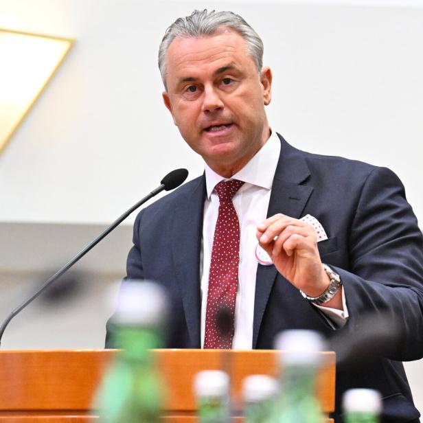 Ein Mann im Anzug spricht an einem Rednerpult mit Mikrofon, im Vordergrund stehen mehrere Flaschen.